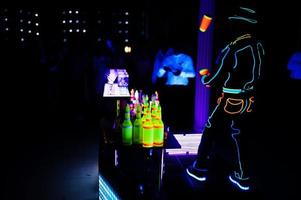 Professional barman and led light show. Silhouette of modern bartender shaking drink at night cocktail bar. photo