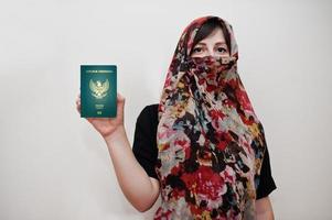 joven musulmana árabe vestida con hijab tiene pasaporte de la república de indonesia sobre fondo de pared blanca, retrato de estudio. foto