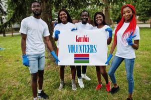 Group of happy african volunteers hold blank with Gambia flag in park. Africa countries volunteering, charity, people and ecology concept. photo