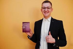 Young handsome man holding Kingdom of Belgium passport id over yellow background, happy and show thumb up. Travel to Europe country concept. photo
