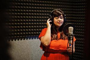 Young asian singer with microphone recording song in record music studio. photo