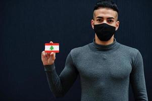 Middle eastern man in gray turtleneck and black face protect mask show Lebanon flag isolated background. photo