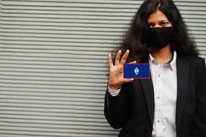 Asian woman at formal wear and black protect face mask hold Guam flag at hand against gray background. Coronavirus at country concept. photo