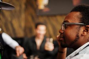 Group of handsome retro well-dressed man gangsters spend time at club, smoking hookah. Multiethnic male bachelor mafia party in restaurant. photo