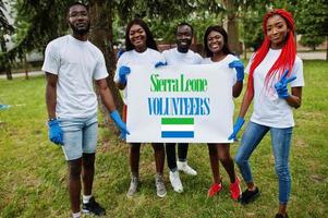 grupo de felices voluntarios africanos se mantienen en blanco con la bandera de sierra leona en el parque. Concepto de voluntariado, caridad, personas y ecología de los países africanos. foto