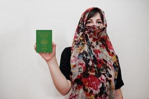 joven musulmana árabe vestida con hiyab tiene pasaporte de la república islámica de mauritania sobre fondo de pared blanca, retrato de estudio. foto