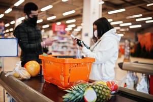 Asian couple wear in protective face mask shopping together in supermarket during pandemic. On the cash register. photo