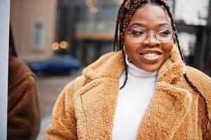 Glamorous african american woman in warm fur coat, eyeglasses pose at street. photo