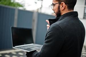 Middle eastern entrepreneur against office building  talk on video call, have web conference with colleagues by laptop. photo