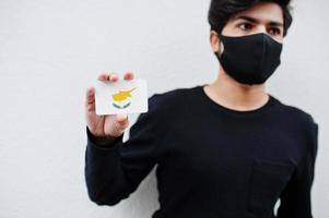 Asian man wear all black with face mask hold Cyprus flag in hand isolated on white background. Coronavirus country concept. photo