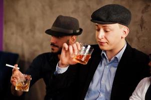 Group of handsome retro well-dressed man gangsters spend time at club, sitting and drinking whiskey. Multiethnic male bachelor mafia party in restaurant. photo