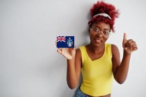 mujer africana con cabello afro, use camiseta amarilla y anteojos, sostenga la bandera de tristán da cunha aislada en fondo blanco, muestre el pulgar hacia arriba. foto