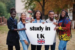 Study in UK. Group of five african college students on campus at university yard hold white blank. Abroad countries for student concept. photo