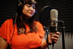 Young asian singer with microphone recording song in record music studio. photo