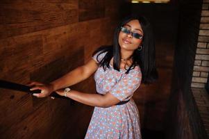 Fashion portrait of african american woman in long dress and eyeglasses indoor. photo