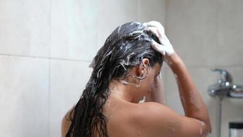 mujer enjabona champú en cabello largo y oscuro en la ducha video