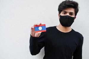 Asian man wear all black with face mask hold Laos flag in hand isolated on white background. Coronavirus country concept. photo