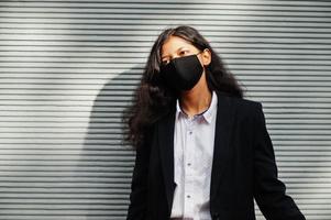 Gorgeous indian woman wear formal and black face mask, posing against wall during covid pandemia. photo