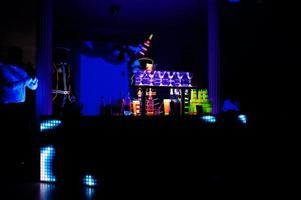 Professional barman and led light show. Silhouette of modern bartender shaking drink at night cocktail bar. photo