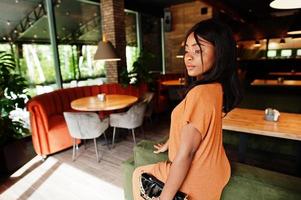 Portrait of beauty young black woman, wear orange outfit, pose at restaurant. photo