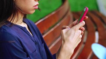 Young brunette woman uses smart phone scrolling and tapping screen on a sitting on a park bench video