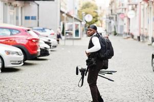 joven camarógrafo afroamericano profesional que sostiene una cámara profesional con equipo profesional de trípode. camarógrafo afro con duraq negro haciendo videos. foto