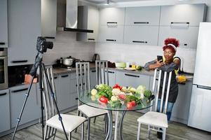 mujer afroamericana filmando la transmisión de su blog sobre comida saludable en la cocina de casa y mirando el teléfono. foto