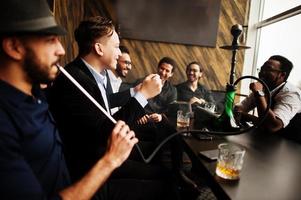 Group of handsome retro well-dressed man gangsters spend time at club, smoking hookah. Multiethnic male bachelor mafia party in restaurant. photo