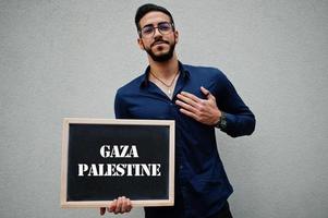 el hombre árabe usa camisa azul y anteojos sostiene una tabla con la inscripción de gaza palestina. ciudades más grandes en el concepto del mundo islámico. foto