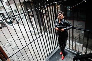 Fashionable beautiful african american woman posing in black leather jacket and pants at street. photo