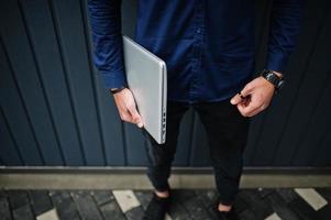 Close up photo of man hands with laptop against steel wall.