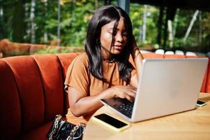 retrato de una joven negra de belleza, vestida de naranja, sentada con una laptop en la oficina. foto