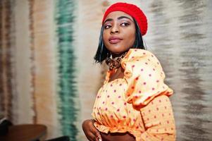 Elegant afro american woman in red french beret, big gold neck chain polka dot blouse pose indoor. photo