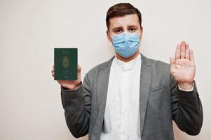 hombre europeo con ropa formal y máscara facial, muestre el pasaporte de las islas feroe con la mano de la señal de stop. bloqueo de coronavirus en el concepto de país de europa. foto