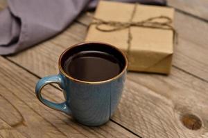 Cup of black coffee on wooden table next to present wrapped into craft paper photo