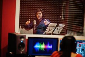 Young asian singer man with microphone recording song in record music studio with sound producer. photo