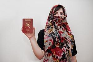 Young arabian muslim woman in hijab clothes hold Sultanate of Oman passport on white wall background, studio portrait. photo