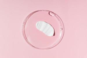 White cosmetic face cream or body lotion moisturizer strokes on pastel pink background in petri dish. Hygiene, skincare product with creamy texture. Beauty face creme smear swatch on color background photo