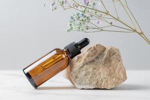 suero facial o aceite esencial en frasco gotero de vidrio oscuro cerca de la piedra y rama seca de la flor de gypsophila. cosmético para el cuidado de la piel. concepto de presentación del producto foto