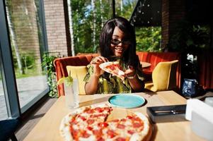 Glamour african american woman eating pizza at restaurant. photo