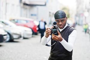 Young professional african american videographer holding professional camera with pro equipment. Afro cameraman wearing black duraq making a videos. photo