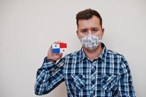 Man in checkered shirt show Panama flag card in hand, wear protect mask isolated on white background. American countries Coronavirus concept. photo