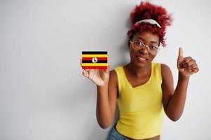 African woman with afro hair, wear yellow singlet and eyeglasses, hold Uganda flag isolated on white background, show thumb up. photo