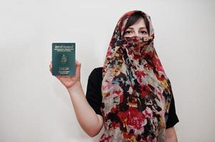 joven musulmana árabe vestida con hiyab tiene pasaporte de la república de túnez sobre fondo de pared blanca, retrato de estudio. foto