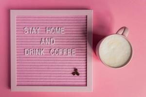 Top view of Pink Coffee cup with cappuccino and qoute Stay home and drink coffee. Self isolation and quarantine campaign to protect yourself from pandemia. photo
