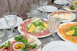mesa festiva, cena familiar con antipasti italiano servido: salmón marinado, jamón, carpaccio, pera, albahaca. paisaje de mesa foto