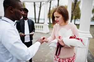 Wedding engagement ceremony with pastor. Multiethnic couple put ring each other. Relationships of african man and white european woman. photo