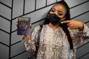 African woman wearing black face mask show Burundi passport in hand. Coronavirus in Africa country, border closure and quarantine, virus outbreak concept. photo