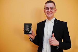 Young handsome man holding New Zealand passport id over yellow background, happy and show thumb up.  Travel to Oceania country concept. photo