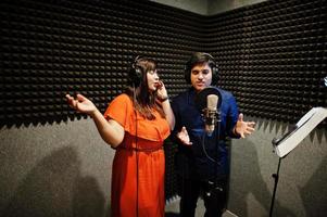 Young asian duet singers with microphone recording song in record music studio. photo